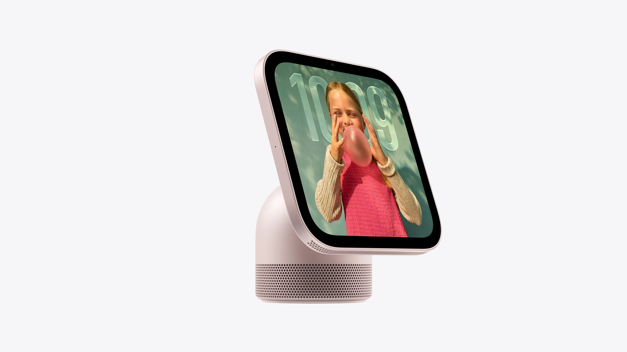 Apple HomeView, rose pink colour, front exterior, rounded corners, flat sides, black display bezel. Microphone on side of display. Circular speaker perforations at bottom of display and on colour-matching cylindrical speaker base. Screen displays photo face and time